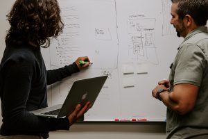 Two people writing the flow of a website on a whiteboard. 