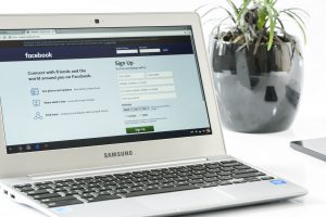 Laptop screen showing Facebook page login window, with plant in background.
