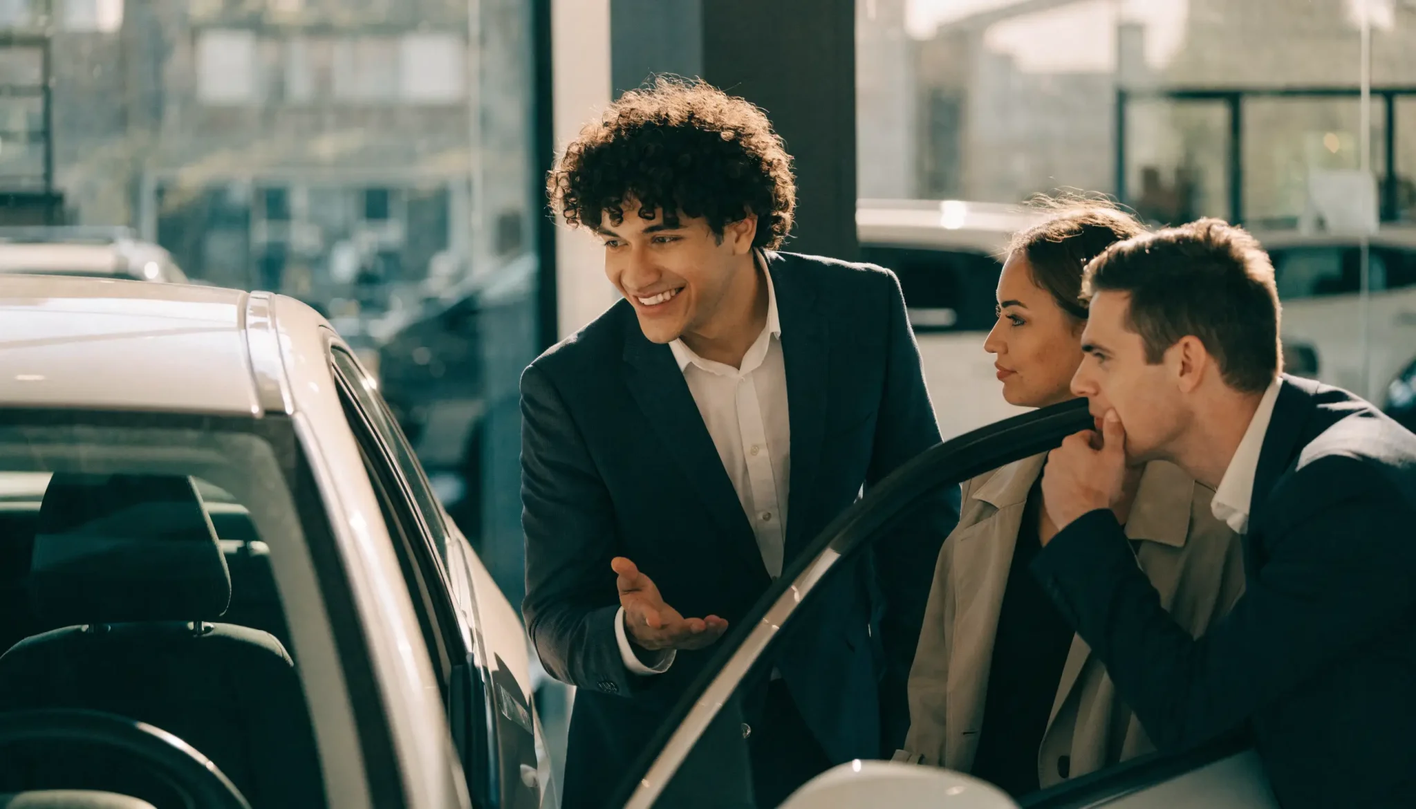 Car salesperson showing a new car to a couple in a dealership showroom